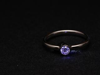 The ring on its own, on a black fabric background with a blue light shining through the diamond.